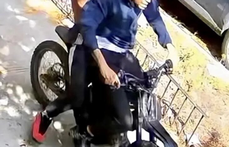 Surveillance footage of two suspects riding a motorized bike on a sidewalk, sought in connection with a robbery.